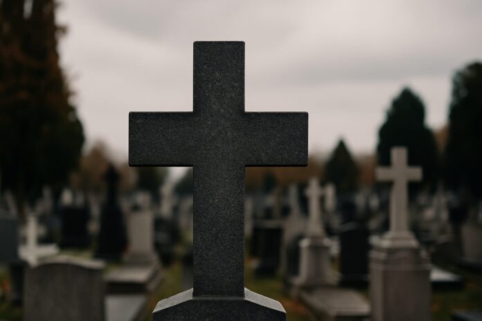 Cruz de granito em cemitério sob céu nublado, simbolizando reflexão sobre herança e despedida
